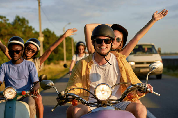 Smiling couple of friends enjoying riding retro scooters on vacation outside the city. Fun, leisure activity, summertime, transportation concept